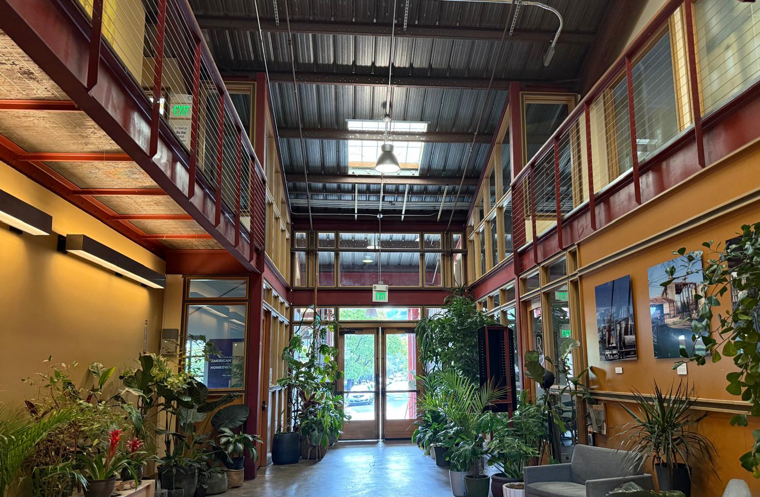 The interior of the old Isaacson Granary in Morgan Hill — a steel-framed industrial building reused as a bright, plant-filled hall, with glass doors opening onto the street